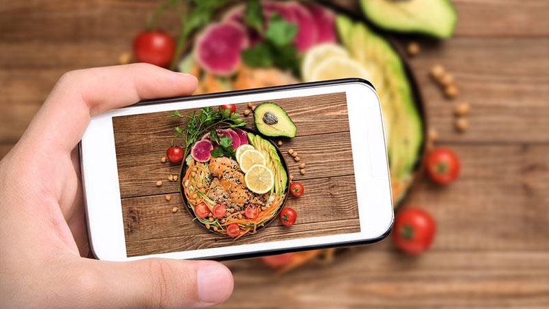 hand taking cell phone picture of healthy fats in salad
